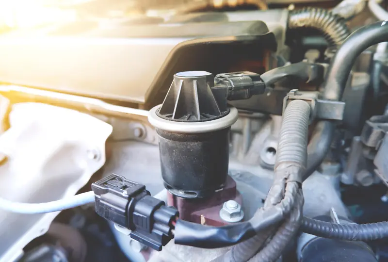 EGR valve showing black cylindrical component with ribbed top section, electrical connector, mounted on metallic bracket in engine bay