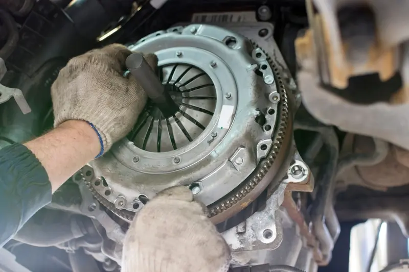Mechanic's hands working on clutch assembly showing pressure plate with diaphragm spring, clutch disc, and flywheel with ring gear