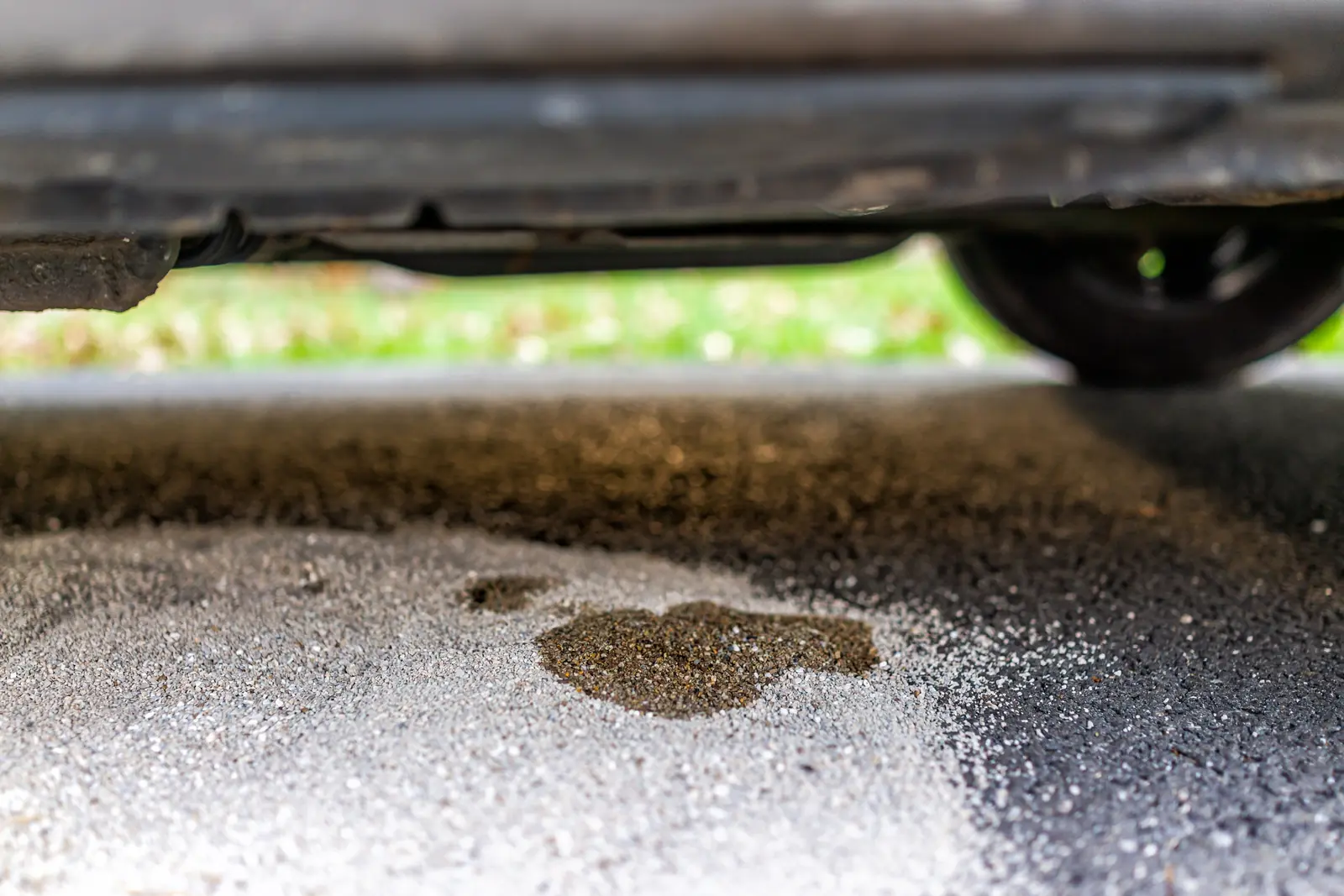 Dark fluid leak puddle on asphalt beneath vehicle undercarriage indicating oil or transmission fluid leak