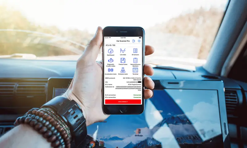 Smartphone displaying OBD diagnostic mobile app interface with car diagnostic icons and functions, shown inside vehicle with dashboard and infotainment screen visible